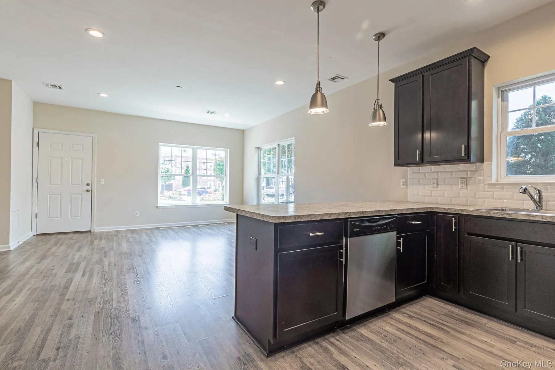 Kitchen featuring a sink, a peninsula, light wood finished floors, backsplash, and stainless steel dishwasher Kitchen featuring a sink, a peninsula, light wood finished floors, backsplash, and stainless steel dishwasher
