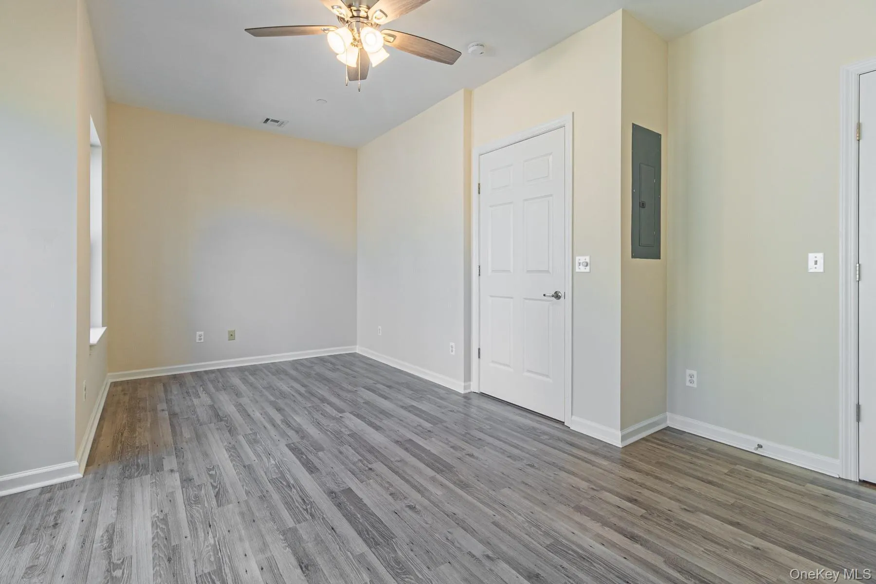 Empty room with visible vents, baseboards, electric panel, a ceiling fan, and wood finished floors Empty room with visible vents, baseboards, electric panel, a ceiling fan, and wood finished floors