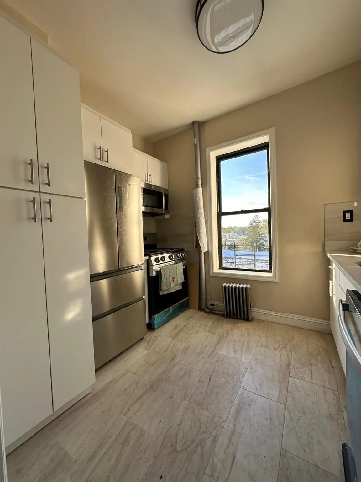 Kitchen featuring baseboards, light countertops, appliances with stainless steel finishes, white cabinetry, and radiator heating unit Kitchen featuring baseboards, light countertops, appliances with stainless steel finishes, white cabinetry, and radiator heating unit