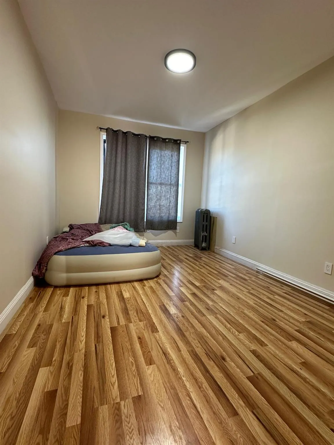 Unfurnished bedroom with wood finished floors, radiator heating unit, and baseboards Unfurnished bedroom with wood finished floors, radiator heating unit, and baseboards