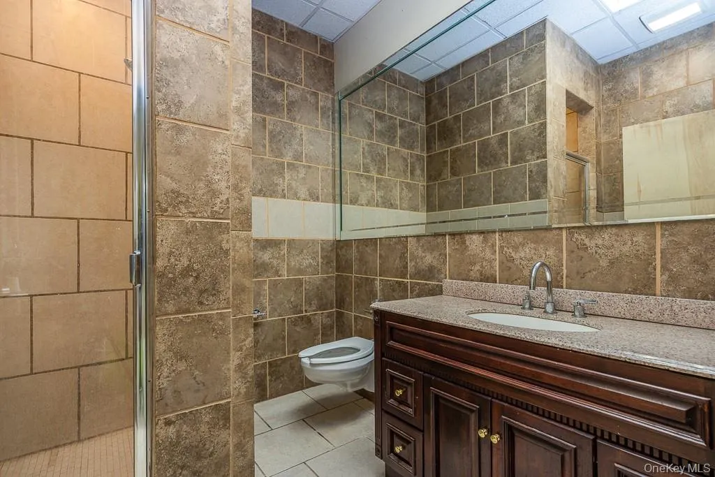 Bathroom with toilet, tile walls, a shower stall, and vanity Bathroom with toilet, tile walls, a shower stall, and vanity