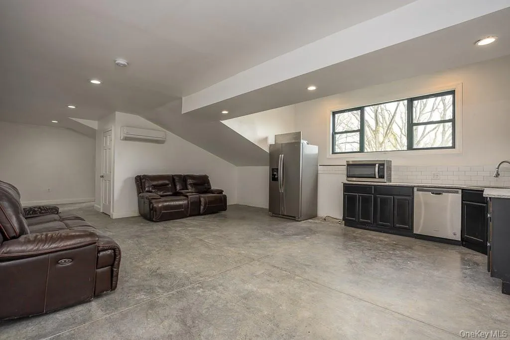 Living area with a wall mounted air conditioner, recessed lighting, vaulted ceiling, and concrete flooring Living area with a wall mounted air conditioner, recessed lighting, vaulted ceiling, and concrete flooring