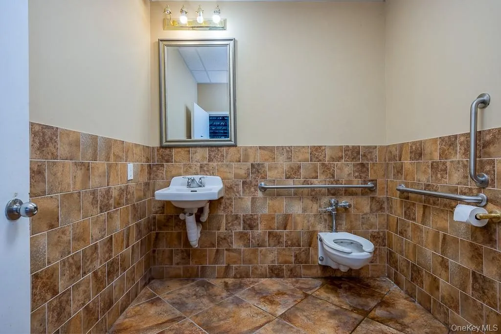 Bathroom with toilet, tile walls, a wainscoted wall, and a sink Bathroom with toilet, tile walls, a wainscoted wall, and a sink