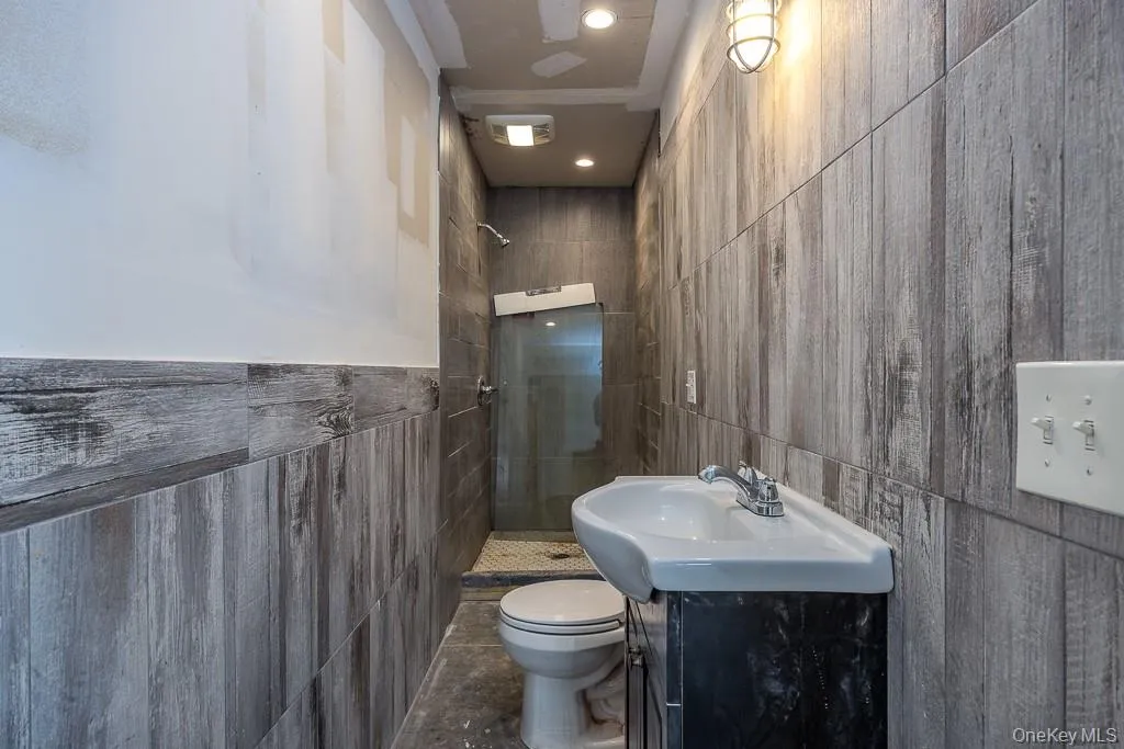 Bathroom with toilet, tile walls, a tile shower, and vanity Bathroom with toilet, tile walls, a tile shower, and vanity