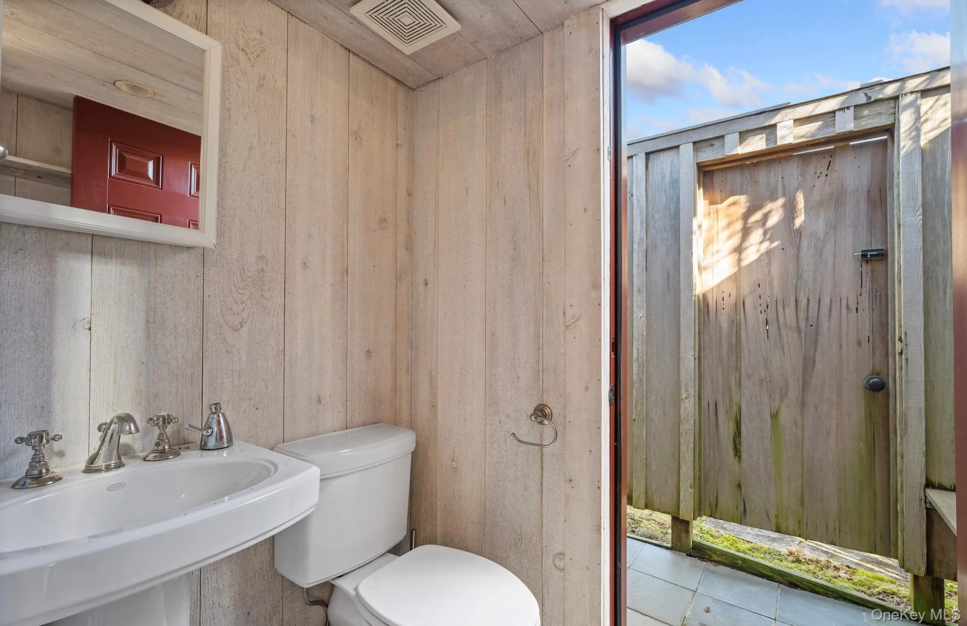 Bathroom featuring a sink, visible vents, toilet, and wooden walls Bathroom featuring a sink, visible vents, toilet, and wooden walls
