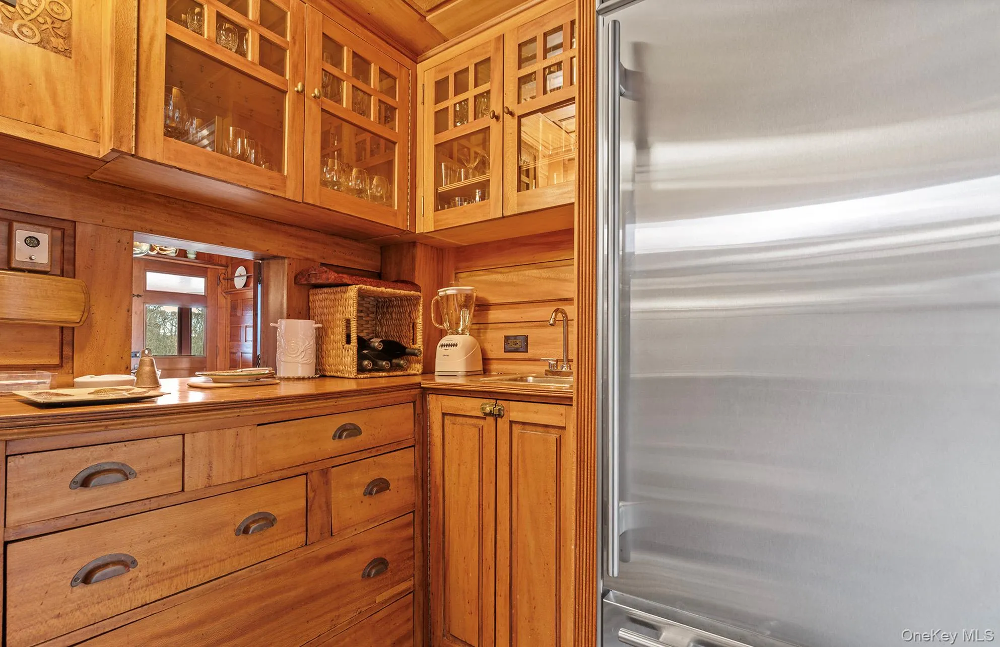 Kitchen featuring glass insert cabinets, a sink, wooden walls, brown cabinetry, and high end refrigerator Kitchen featuring glass insert cabinets, a sink, wooden walls, brown cabinetry, and high end refrigerator