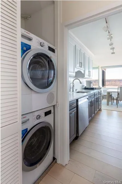 Laundry area with stacked washing maching and dryer, laundry area, a sink, and rail lighting Laundry area with stacked washing maching and dryer, laundry area, a sink, and rail lighting