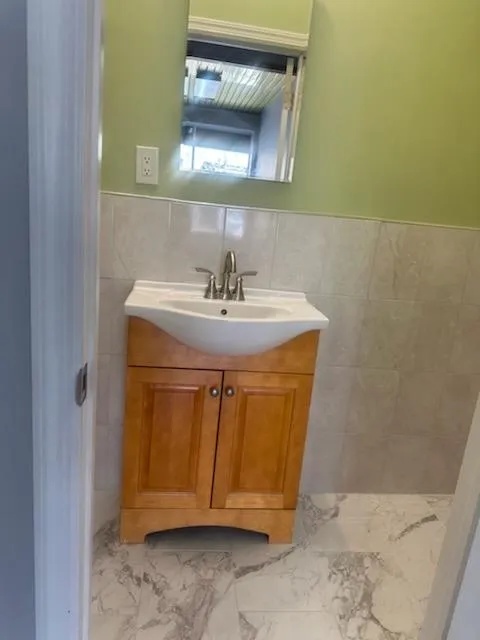 Bathroom with tile walls, marble finish floor, vanity, and a wainscoted wall Bathroom with tile walls, marble finish floor, vanity, and a wainscoted wall