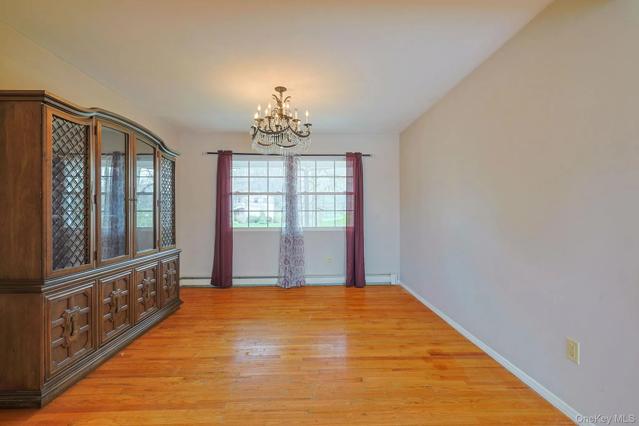 This room features hardwood floors, a prominent window providing natural light, and an overhead chandelier This room features hardwood floors, a prominent window providing natural light, and an overhead chandelier