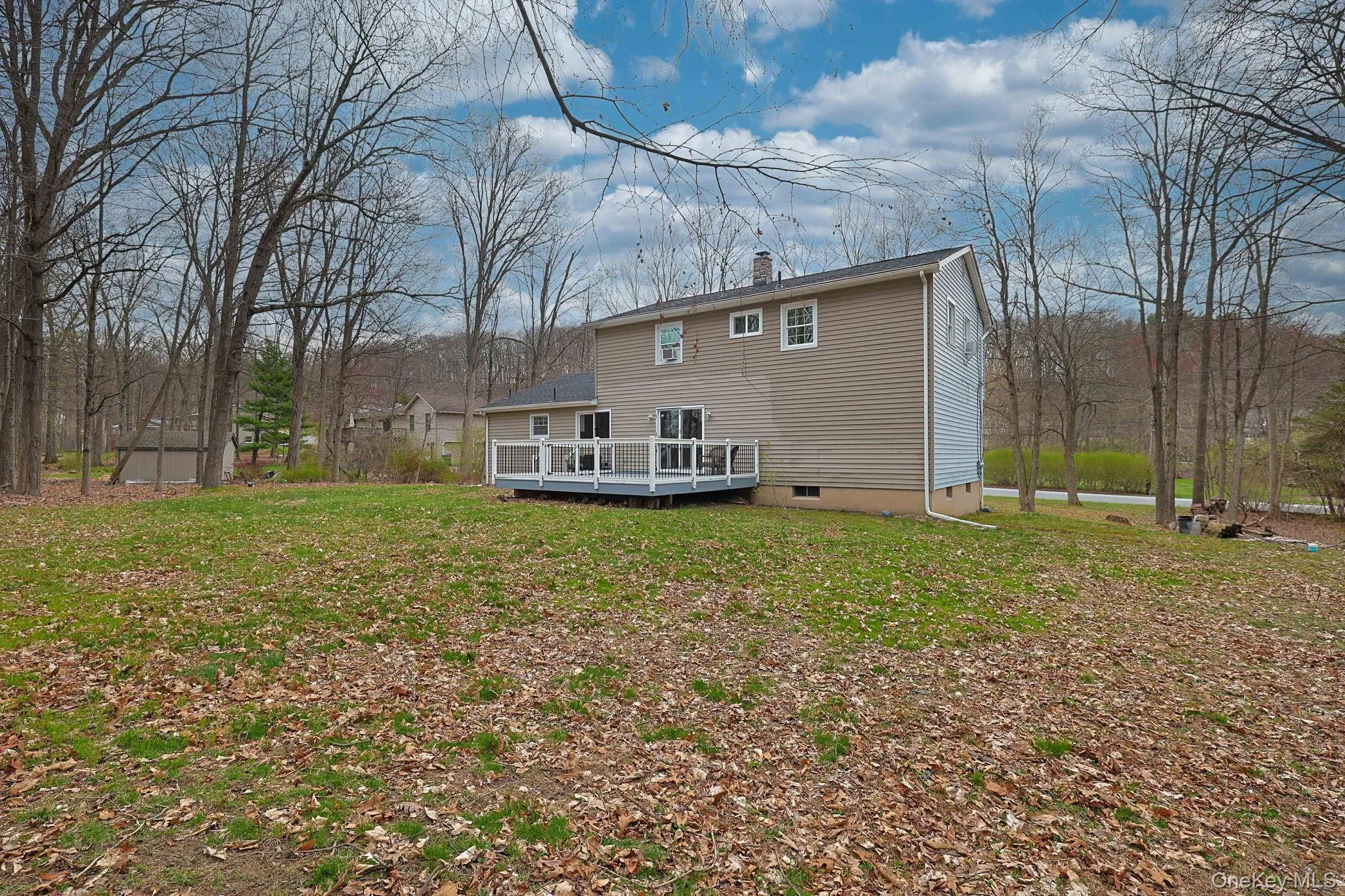 The property features a spacious yard with a mix of green grass and fallen leaves, surrounded by mature trees The property features a spacious yard with a mix of green grass and fallen leaves, surrounded by mature trees