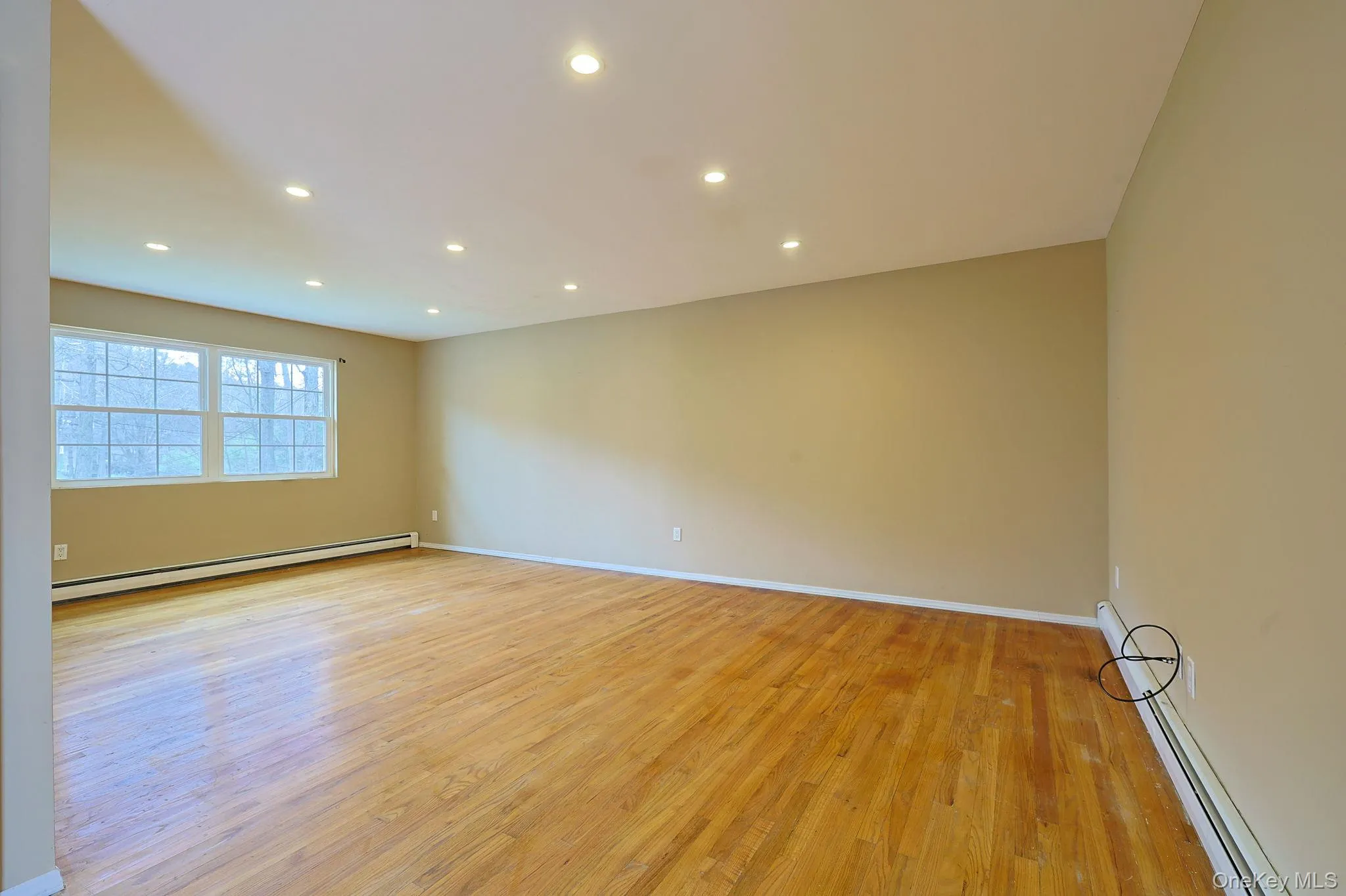 Spacious room featuring hardwood floors, recessed lighting, and large windows providing views of exterior trees Spacious room featuring hardwood floors, recessed lighting, and large windows providing views of exterior trees