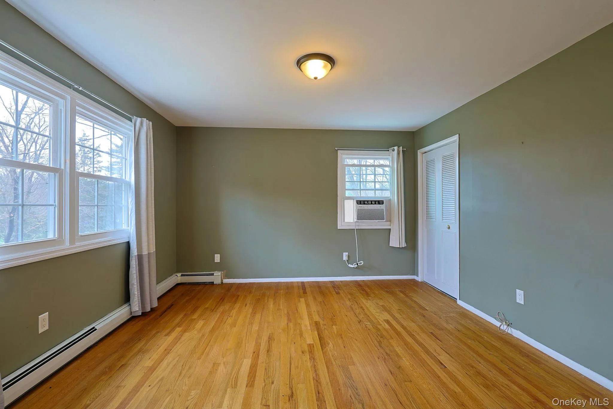 The room features hardwood floors, a ceiling light fixture, and windows providing natural light The room features hardwood floors, a ceiling light fixture, and windows providing natural light