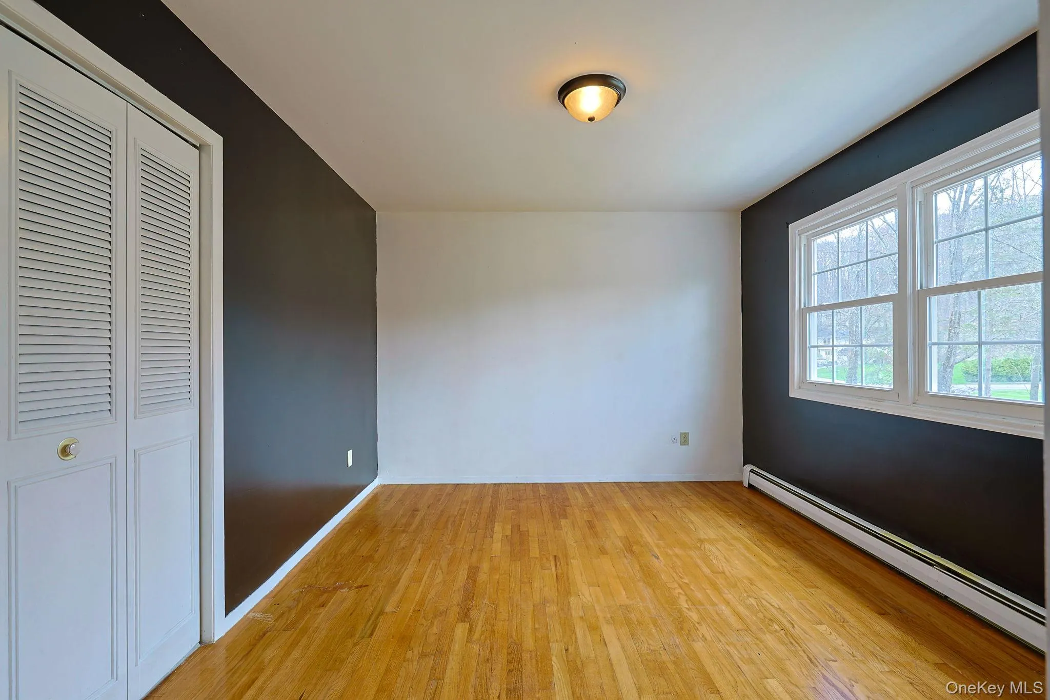 This room features hardwood flooring, a ceiling-mounted light fixture, and two windows providing natural light This room features hardwood flooring, a ceiling-mounted light fixture, and two windows providing natural light