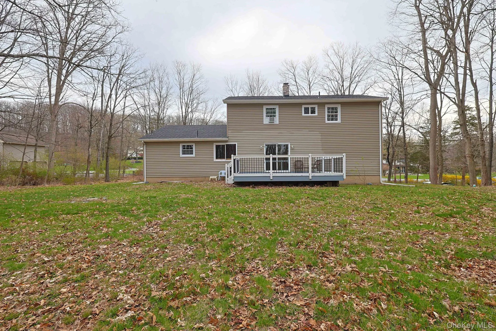 The property features a spacious rear yard with a green lawn, a deck, and mature trees surrounding the perimeter The property features a spacious rear yard with a green lawn, a deck, and mature trees surrounding the perimeter