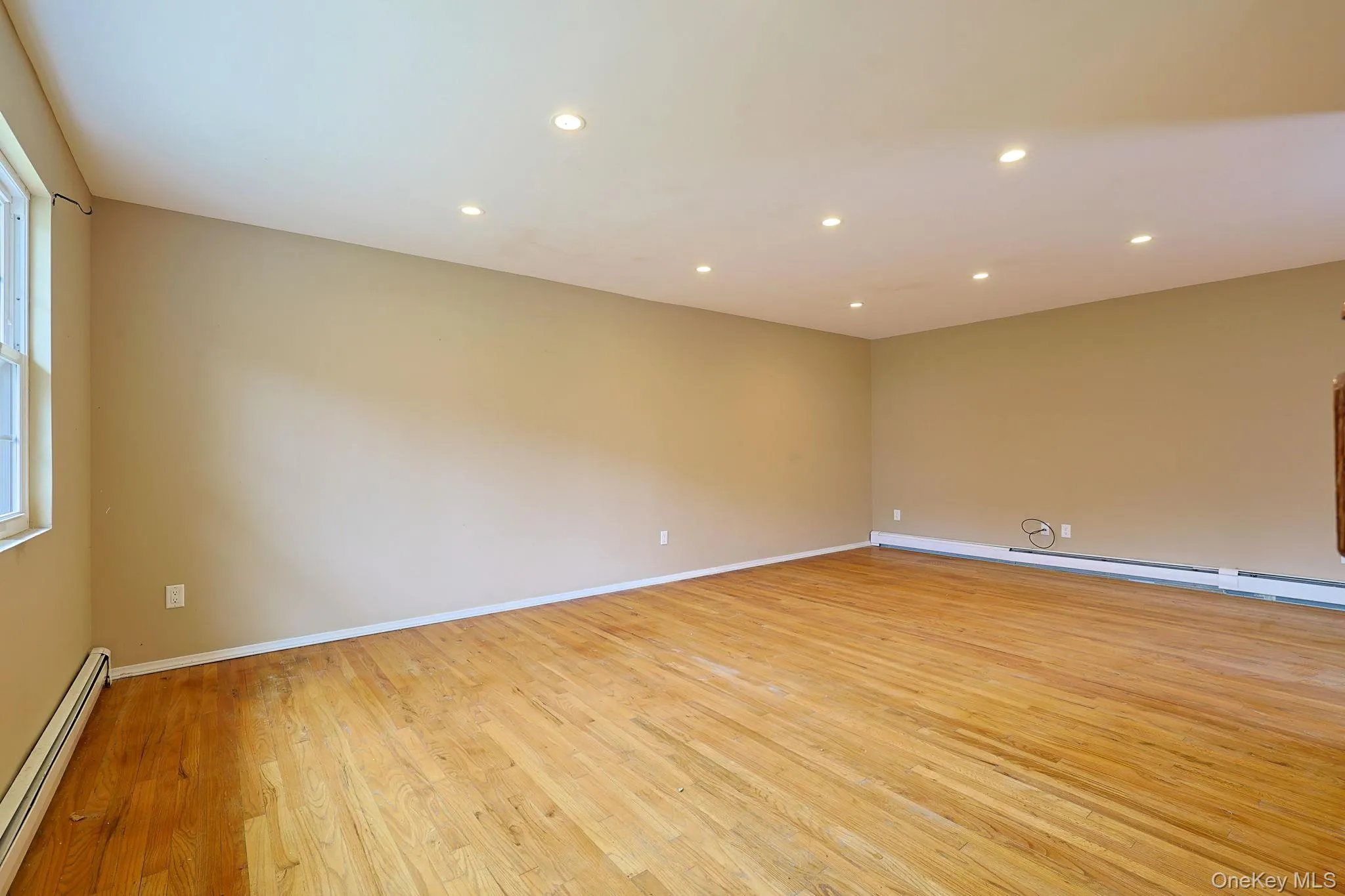 Spacious room with hardwood floors, recessed lighting, and a window for natural light Spacious room with hardwood floors, recessed lighting, and a window for natural light