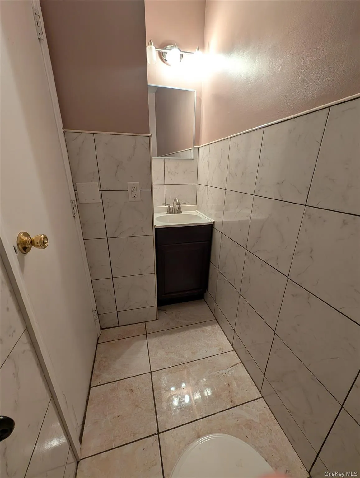 Bathroom featuring tiled flooring and walls, a vanity with a dark wood cabinet, and a wall-mounted light fixture Bathroom featuring tiled flooring and walls, a vanity with a dark wood cabinet, and a wall-mounted light fixture