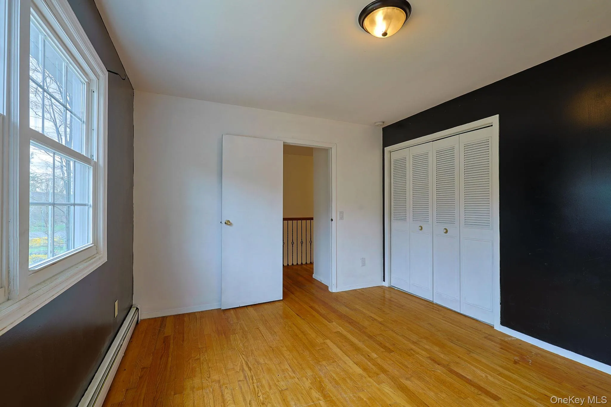 This room features hardwood floors, a window with natural light, a closet with bi-fold louvered doors, and a ceiling-mounted light fixture This room features hardwood floors, a window with natural light, a closet with bi-fold louvered doors, and a ceiling-mounted light fixture