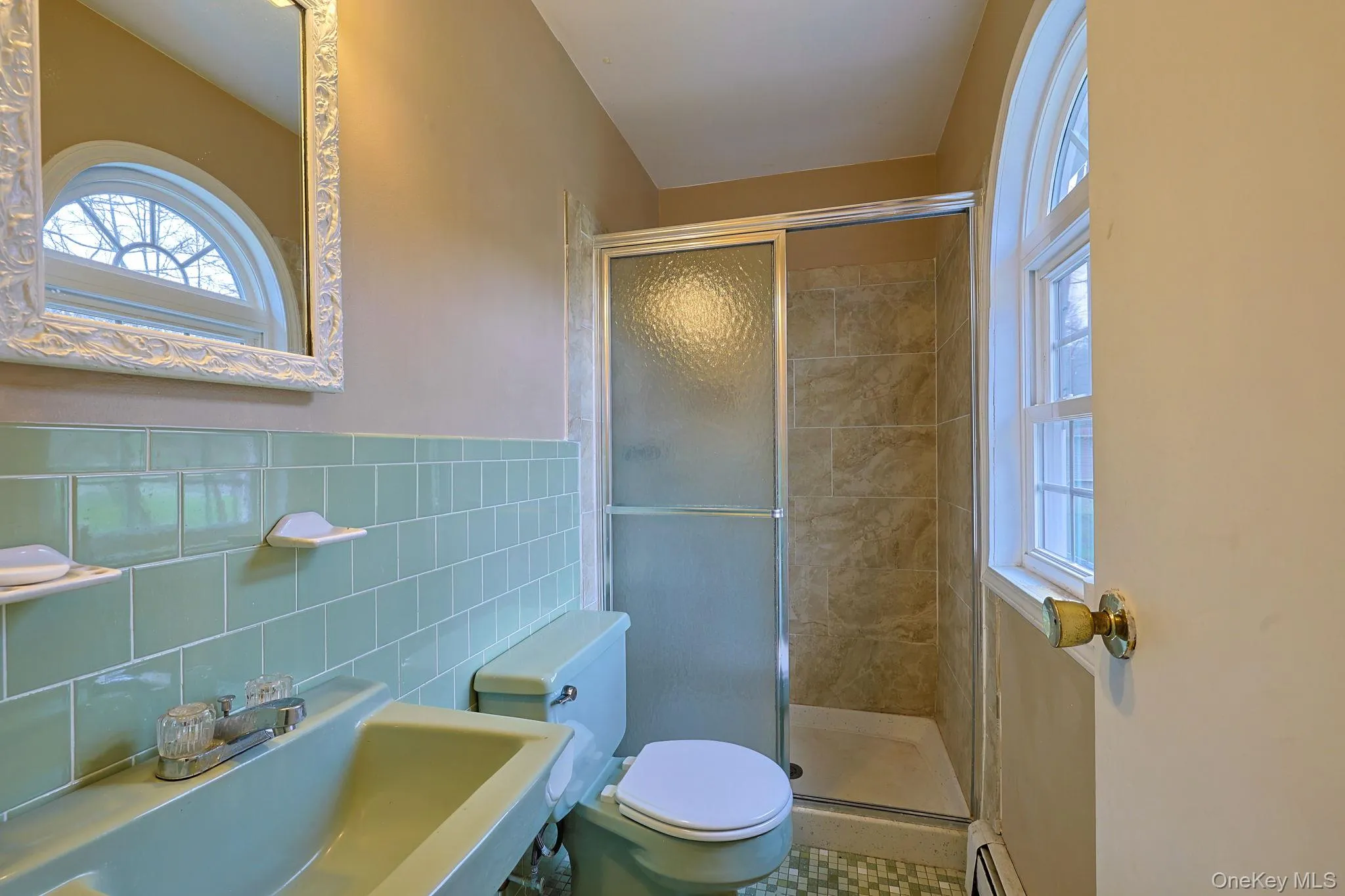 Bathroom featuring a shower with sliding glass doors, a window with an arched top, and a sink with a mirror Bathroom featuring a shower with sliding glass doors, a window with an arched top, and a sink with a mirror