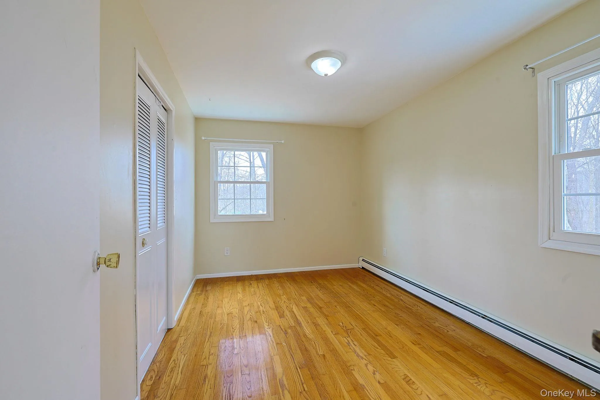 This room features hardwood floors, a ceiling light fixture, and two windows providing natural light This room features hardwood floors, a ceiling light fixture, and two windows providing natural light