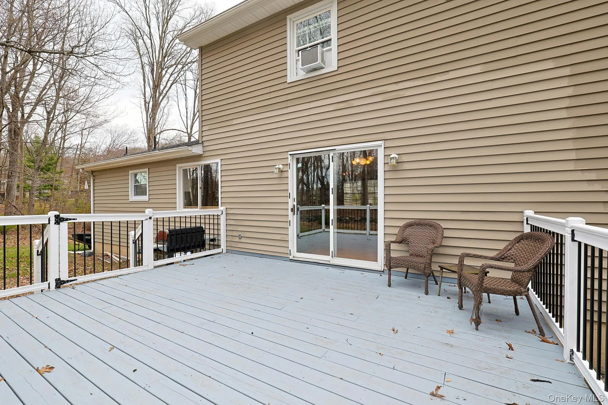 An expansive outdoor deck featuring white railings with black balusters, providing direct access to the interior via sliding glass doors An expansive outdoor deck featuring white railings with black balusters, providing direct access to the interior via sliding glass doors