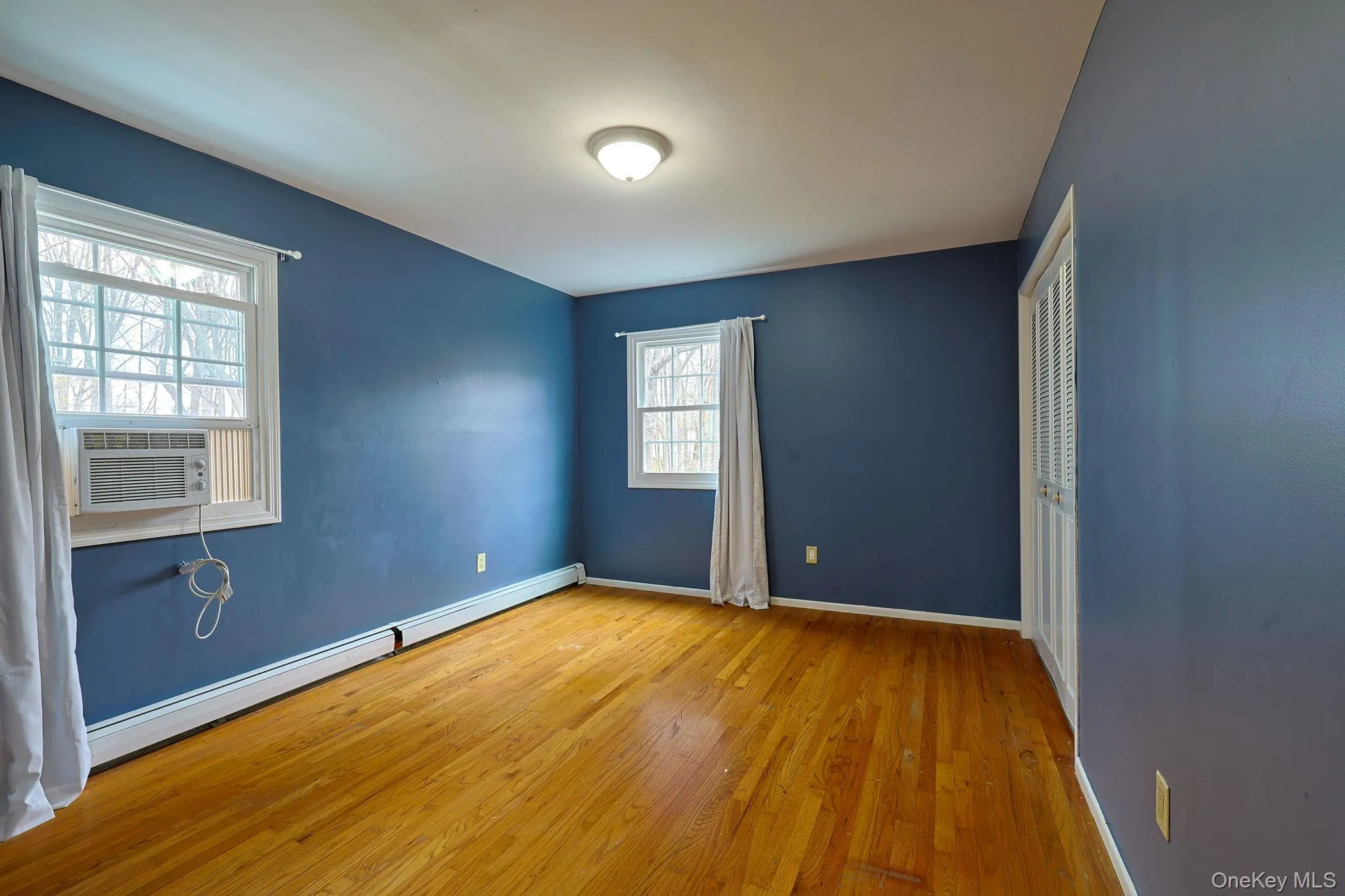 This room features hardwood floors, a ceiling light fixture, and two windows providing natural light This room features hardwood floors, a ceiling light fixture, and two windows providing natural light