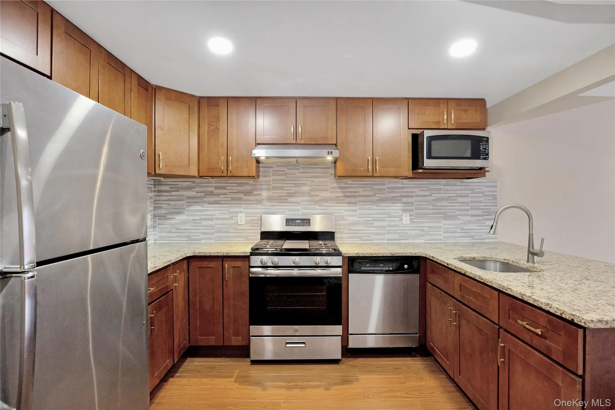 Kitchen featuring appliances with stainless steel finishes, light wood finished floors, a sink, and under cabinet range hood Kitchen featuring appliances with stainless steel finishes, light wood finished floors, a sink, and under cabinet range hood