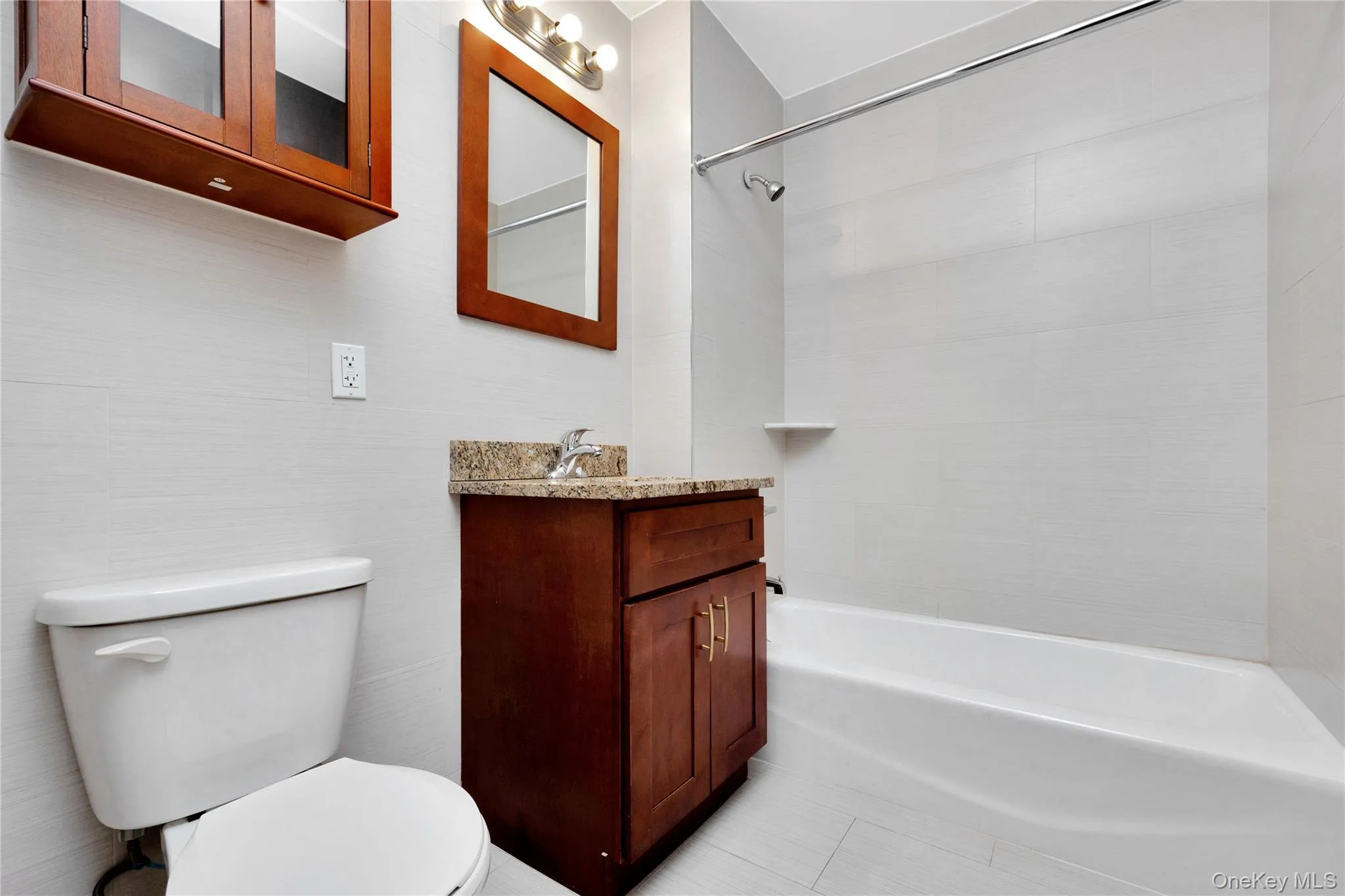 Full bathroom featuring vanity, shower combination, toilet, tile walls, and tile patterned floors Full bathroom featuring vanity, shower combination, toilet, tile walls, and tile patterned floors