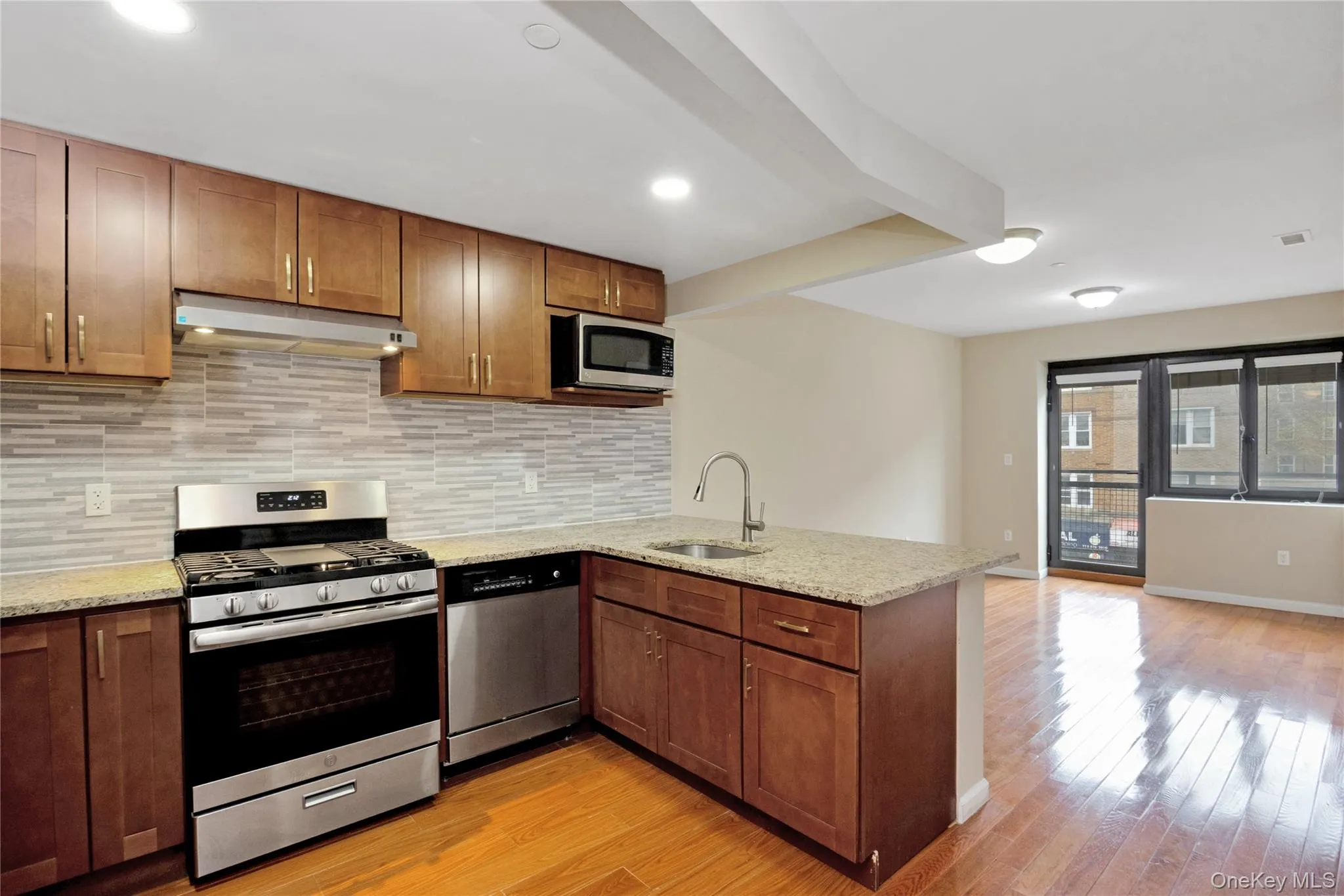 Kitchen featuring a peninsula, appliances with stainless steel finishes, under cabinet range hood, a sink, and backsplash Kitchen featuring a peninsula, appliances with stainless steel finishes, under cabinet range hood, a sink, and backsplash