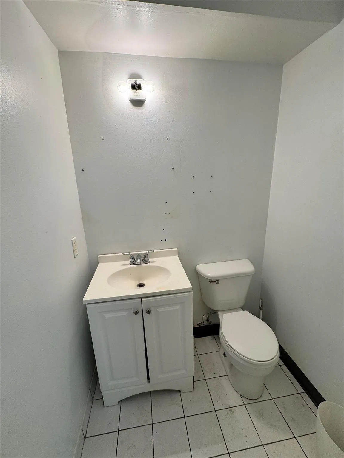 Half bathroom featuring tile patterned flooring, toilet, vanity, and baseboards Half bathroom featuring tile patterned flooring, toilet, vanity, and baseboards