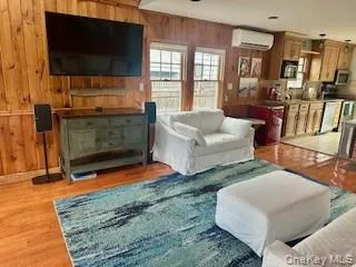 Living area with wood finished floors, wooden walls, and an AC wall unit Living area with wood finished floors, wooden walls, and an AC wall unit