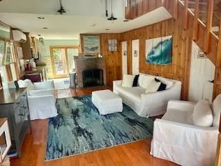 Living area featuring wood finished floors, wooden walls, a wall mounted air conditioner, a fireplace, and a high ceiling Living area featuring wood finished floors, wooden walls, a wall mounted air conditioner, a fireplace, and a high ceiling