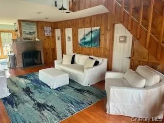 Living room featuring wood walls, wood finished floors, a ceiling fan, and a brick fireplace Living room featuring wood walls, wood finished floors, a ceiling fan, and a brick fireplace