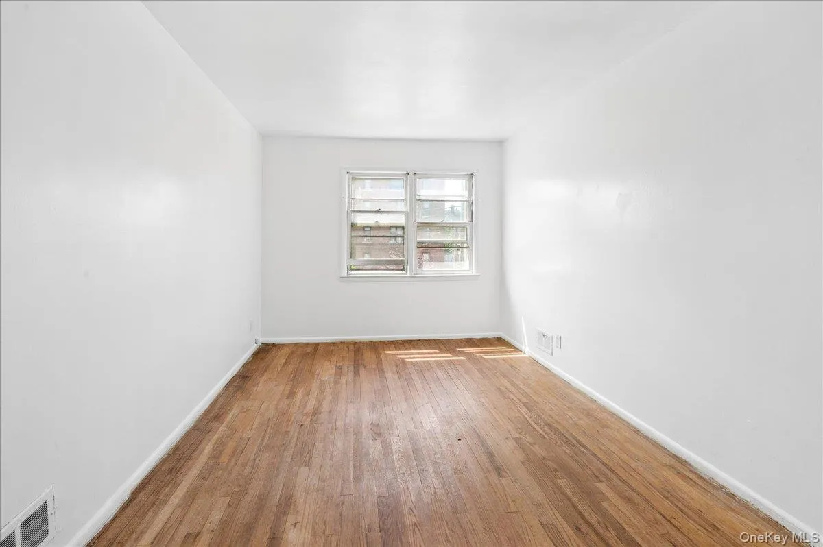 Bright room featuring wood-finish flooring, white painted walls, and a double-hung window Bright room featuring wood-finish flooring, white painted walls, and a double-hung window