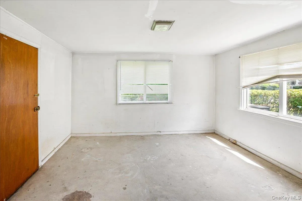 White-painted interior space featuring a wood-finish door, two windows, and a ceiling-mounted light fixture White-painted interior space featuring a wood-finish door, two windows, and a ceiling-mounted light fixture