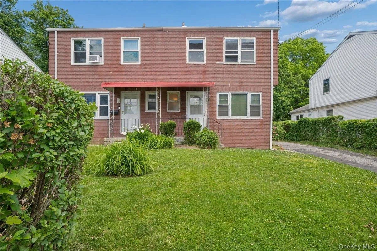 Brick facade structure with a red awning over dual entryways, featuring a front lawn and a paved driveway Brick facade structure with a red awning over dual entryways, featuring a front lawn and a paved driveway