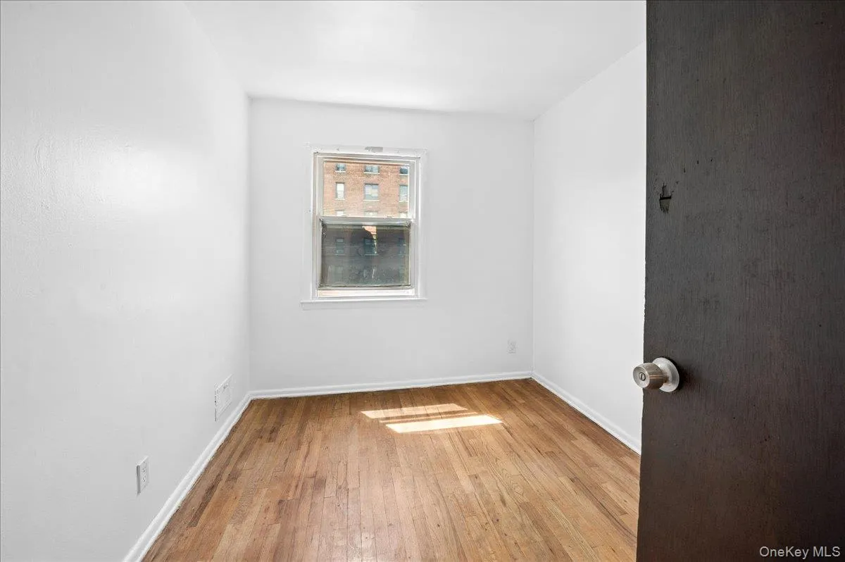 Room featuring hardwood flooring, white baseboards, and a single window with white trim Room featuring hardwood flooring, white baseboards, and a single window with white trim