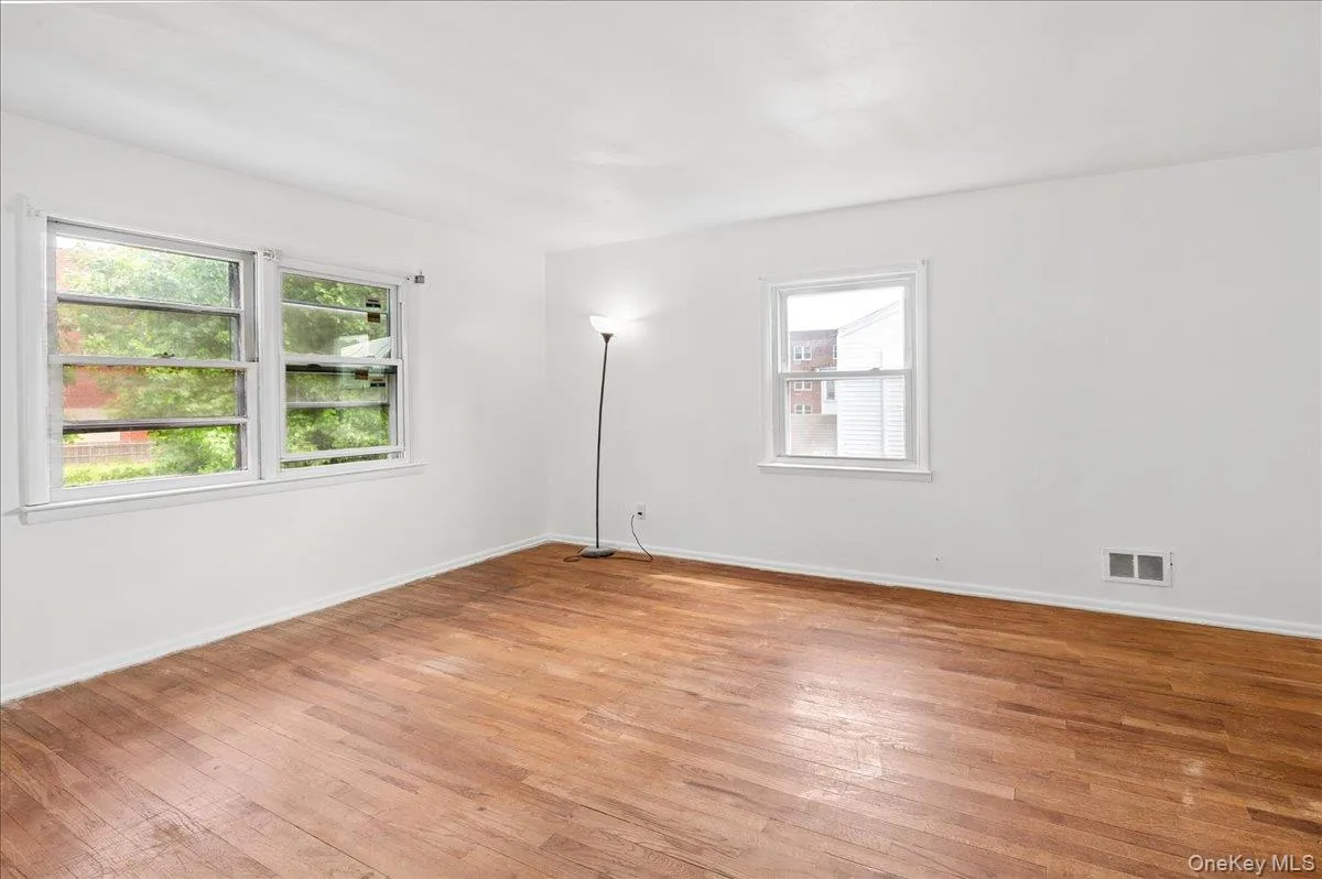 Spacious room featuring wood-finish flooring, white walls, and multiple windows Spacious room featuring wood-finish flooring, white walls, and multiple windows