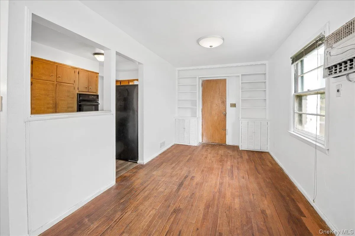 Hardwood flooring throughout the room, with a pass-through opening to the kitchen featuring wood cabinetry and a black refrigerator Hardwood flooring throughout the room, with a pass-through opening to the kitchen featuring wood cabinetry and a black refrigerator