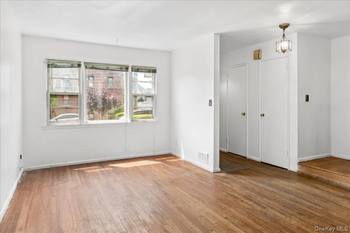 Living area featuring wood-finish flooring, white walls, and a multi-pane window Living area featuring wood-finish flooring, white walls, and a multi-pane window