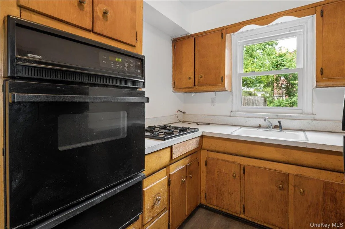 Kitchen featuring a built-in black double oven, integrated gas cooktop, natural wood cabinetry, a single basin sink, and a window Kitchen featuring a built-in black double oven, integrated gas cooktop, natural wood cabinetry, a single basin sink, and a window