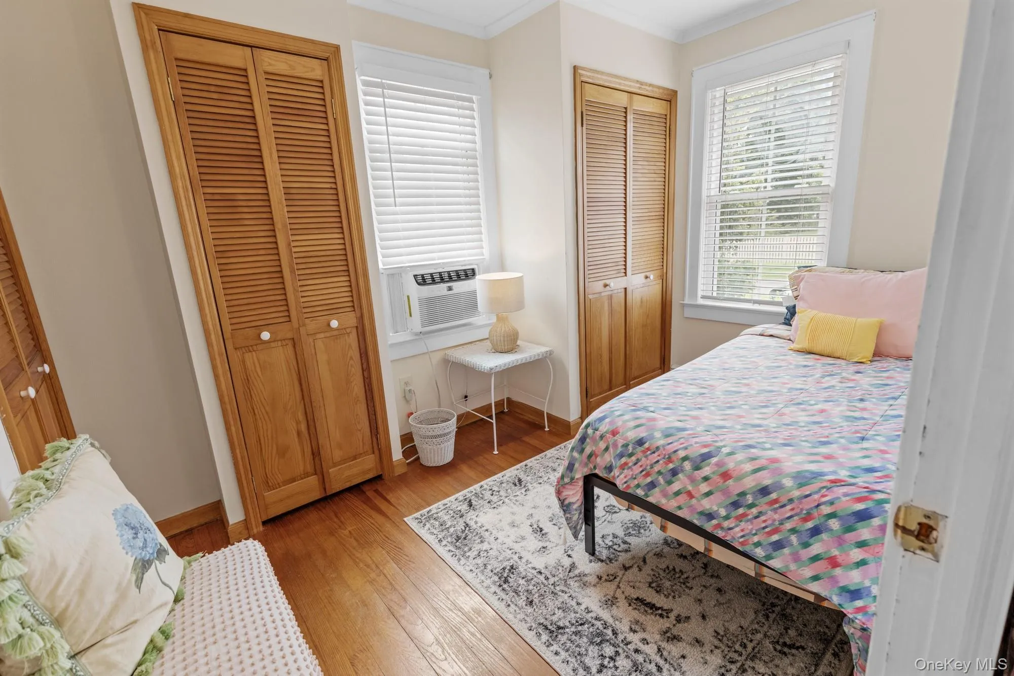 Bedroom with multiple closets, ornamental molding, light wood-style flooring, and cooling unit Bedroom with multiple closets, ornamental molding, light wood-style flooring, and cooling unit