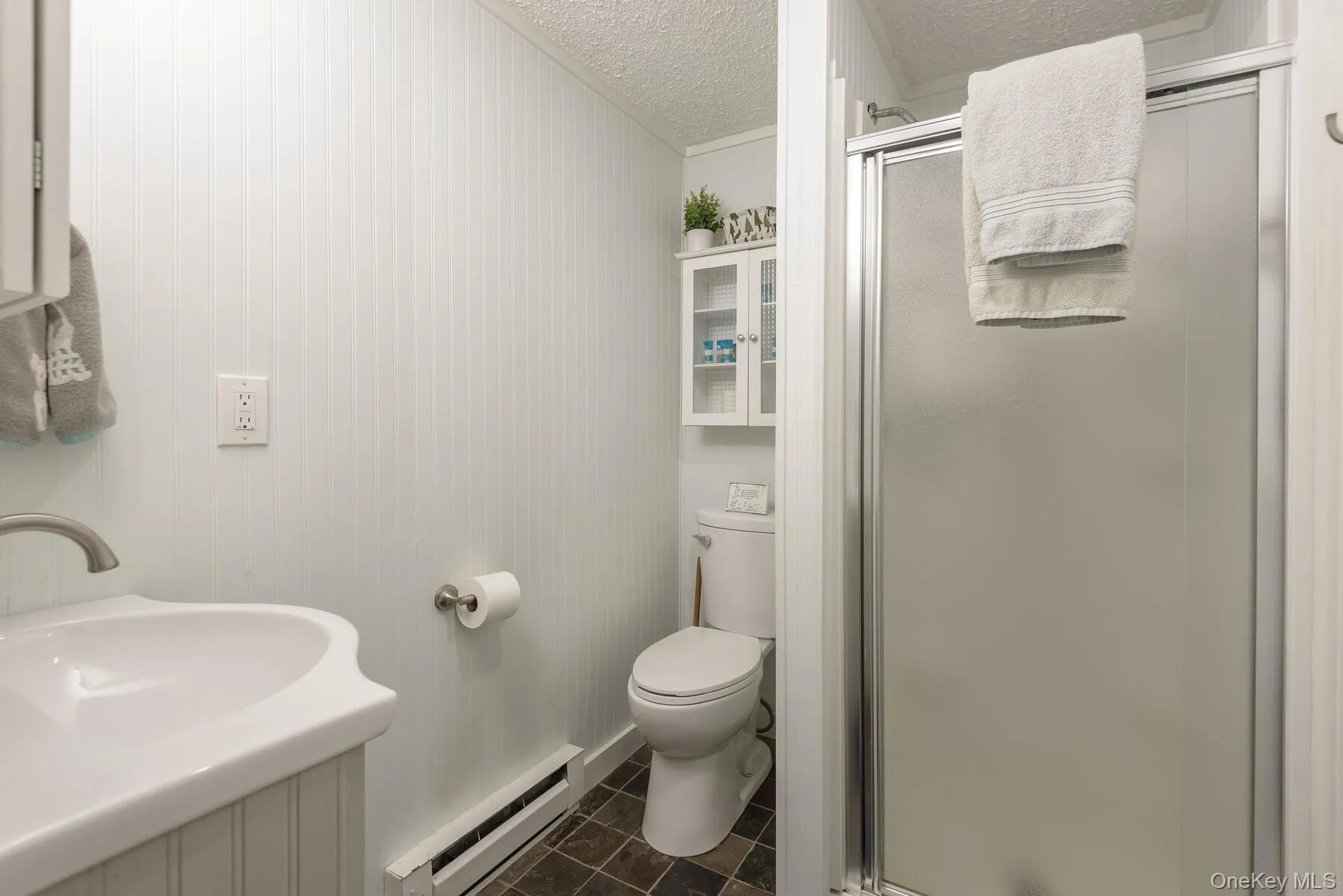 Bathroom featuring toilet, a baseboard radiator, a shower stall, and a textured ceiling Bathroom featuring toilet, a baseboard radiator, a shower stall, and a textured ceiling