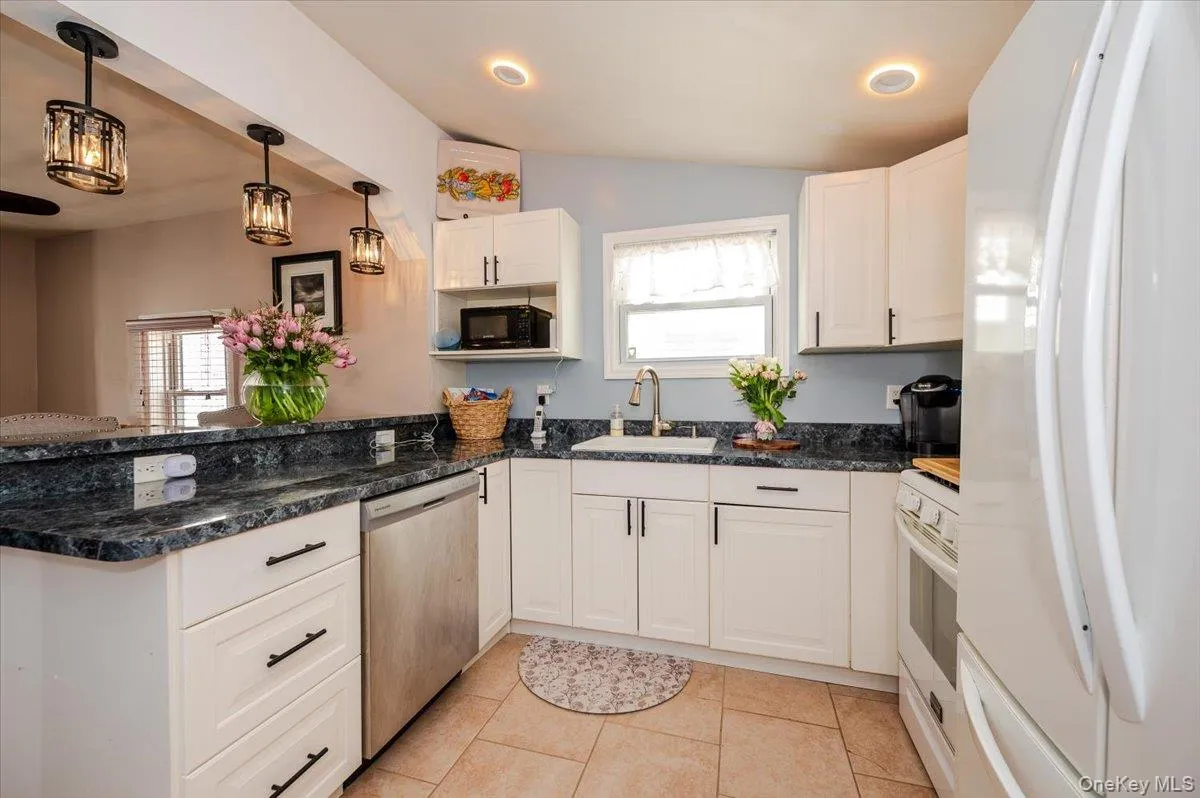 Kitchen with hanging light fixtures, a sink, white appliances, white cabinets, and a peninsula Kitchen with hanging light fixtures, a sink, white appliances, white cabinets, and a peninsula