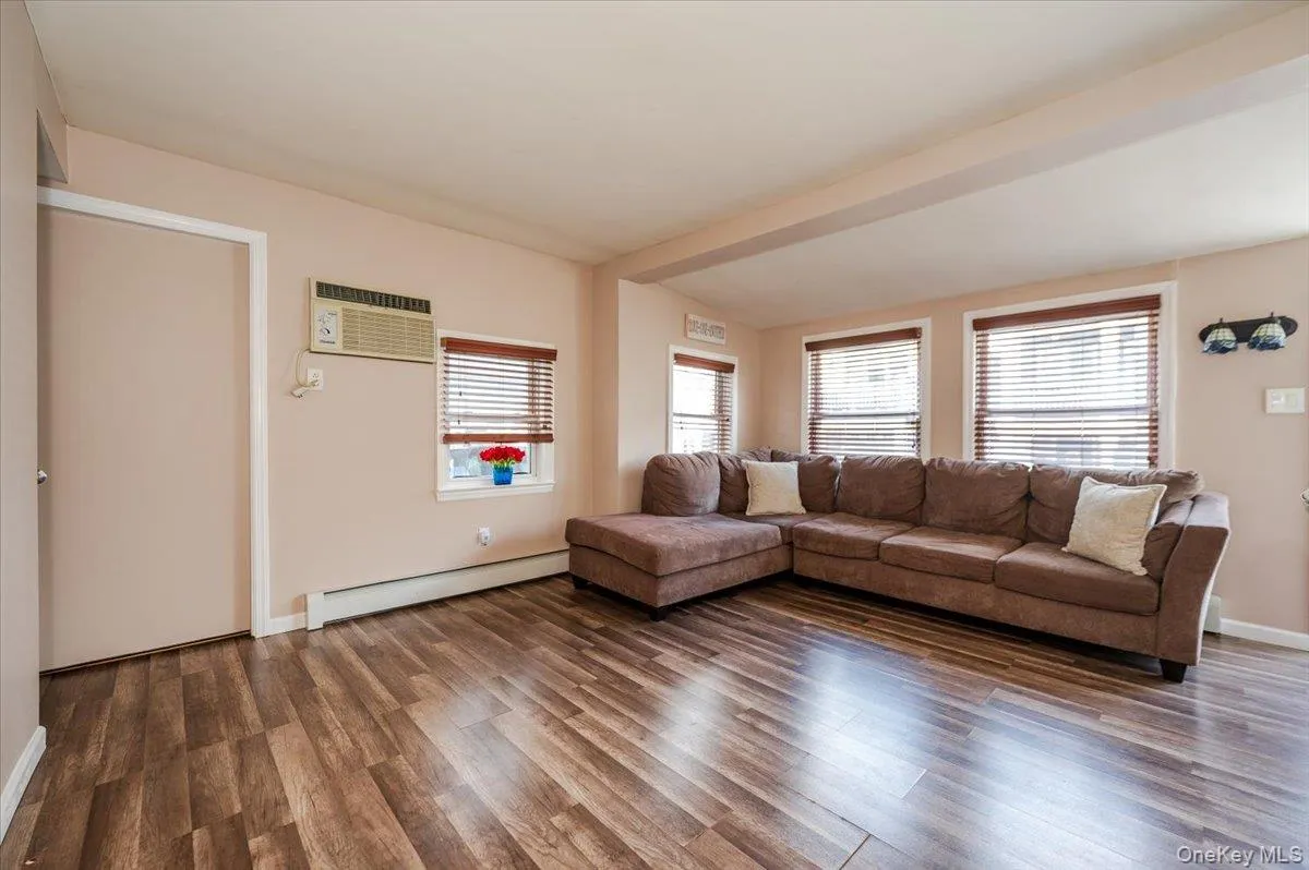 Living area featuring a baseboard heating unit, a wall mounted AC, wood finished floors, and a wealth of natural light Living area featuring a baseboard heating unit, a wall mounted AC, wood finished floors, and a wealth of natural light