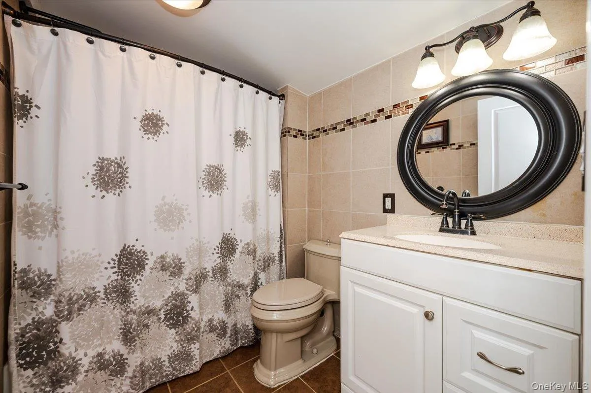 Full bath with a shower with curtain, toilet, tile walls, tile patterned flooring, and vanity Full bath with a shower with curtain, toilet, tile walls, tile patterned flooring, and vanity