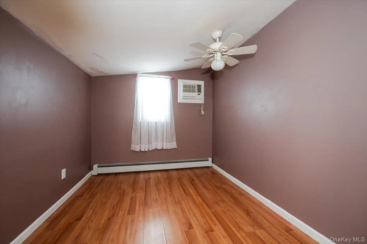 Unfurnished room with an AC wall unit, vaulted ceiling, a baseboard heating unit, light wood-style flooring, and baseboards Unfurnished room with an AC wall unit, vaulted ceiling, a baseboard heating unit, light wood-style flooring, and baseboards