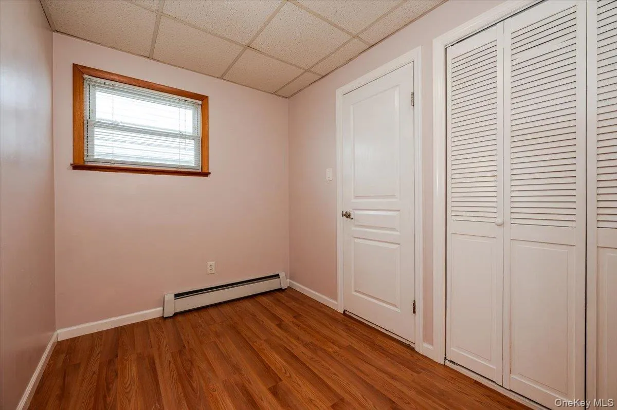 Unfurnished bedroom with a baseboard heating unit, light wood-style floors, a drop ceiling, and baseboards Unfurnished bedroom with a baseboard heating unit, light wood-style floors, a drop ceiling, and baseboards