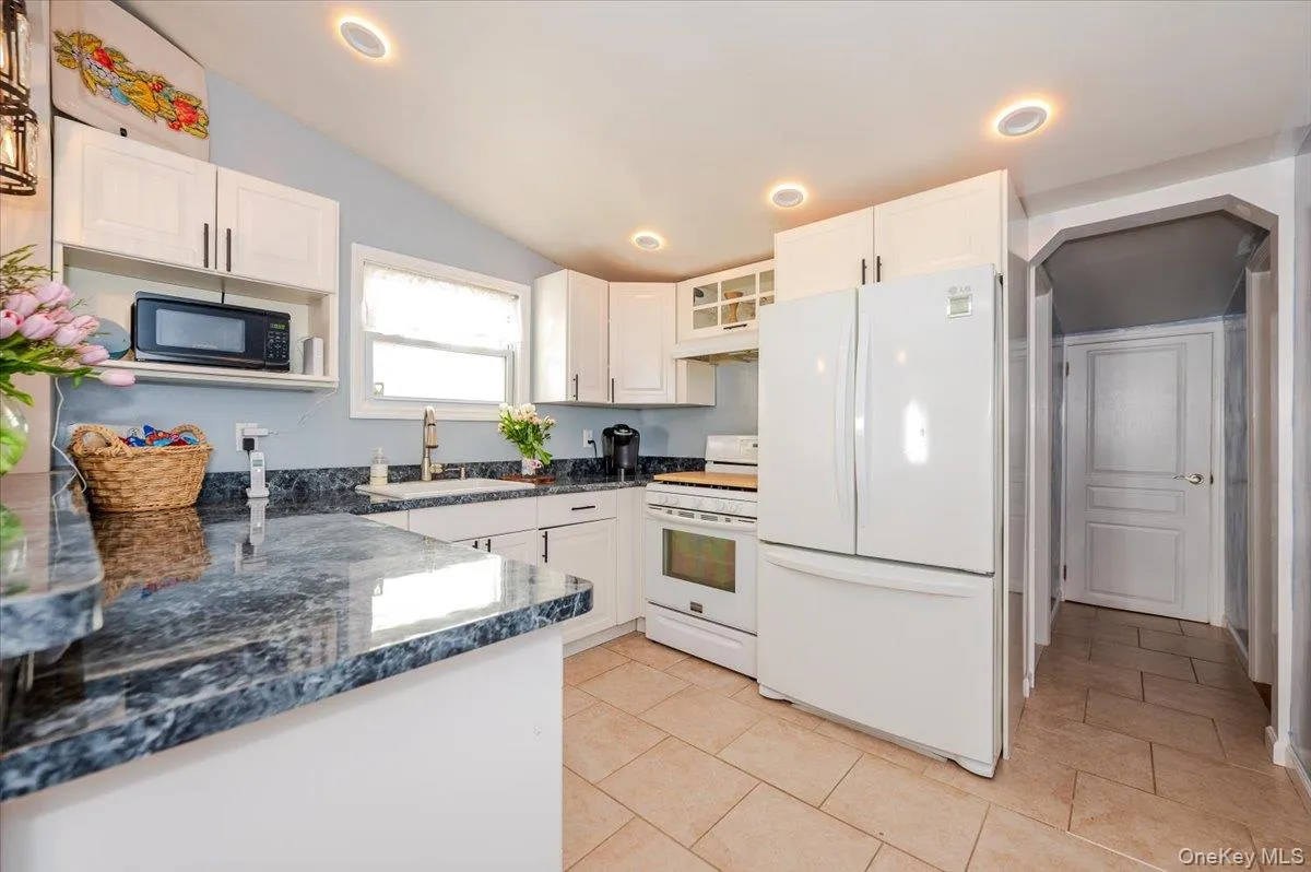Kitchen with vaulted ceiling, a sink, under cabinet range hood, white appliances, and white cabinetry Kitchen with vaulted ceiling, a sink, under cabinet range hood, white appliances, and white cabinetry