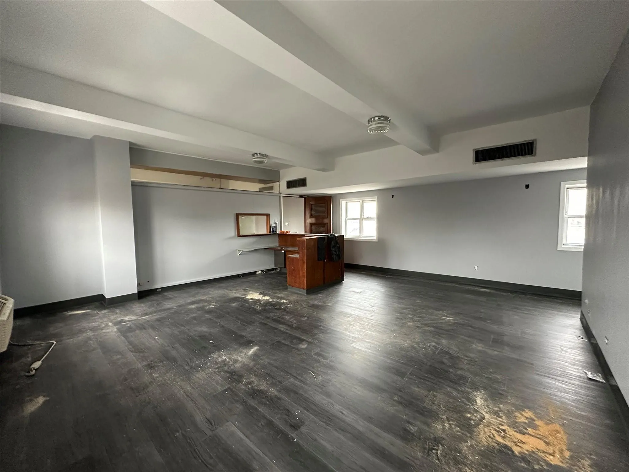 Unfurnished living room with dark wood-type flooring, visible vents, baseboards, and beam ceiling Unfurnished living room with dark wood-type flooring, visible vents, baseboards, and beam ceiling