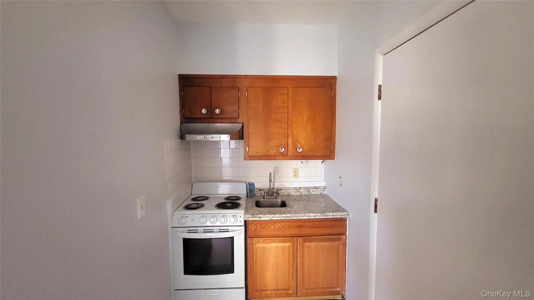 Kitchen featuring range hood, backsplash, a sink, brown cabinetry, and electric range Kitchen featuring range hood, backsplash, a sink, brown cabinetry, and electric range